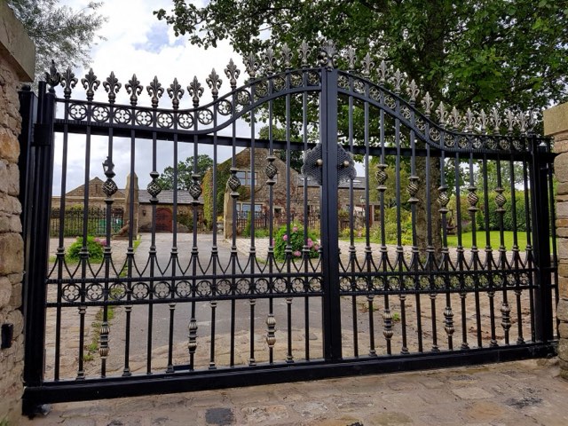Automatic wrought iron driveway gates with fleur-de-lis finials between stone pillars