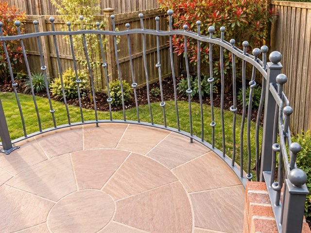 Curved wrought iron garden railings with ball finials around a patio