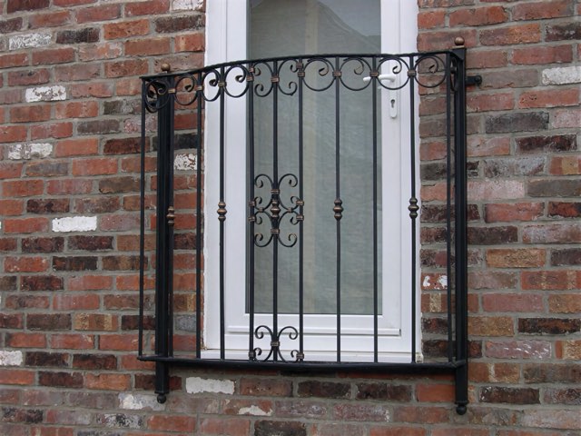 Wrought iron Juliet balcony with scrollwork and copper-finish details on a brick house