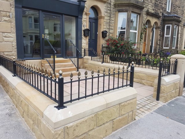 Wrought iron front garden railings with bronze flame finials on a sandstone wall